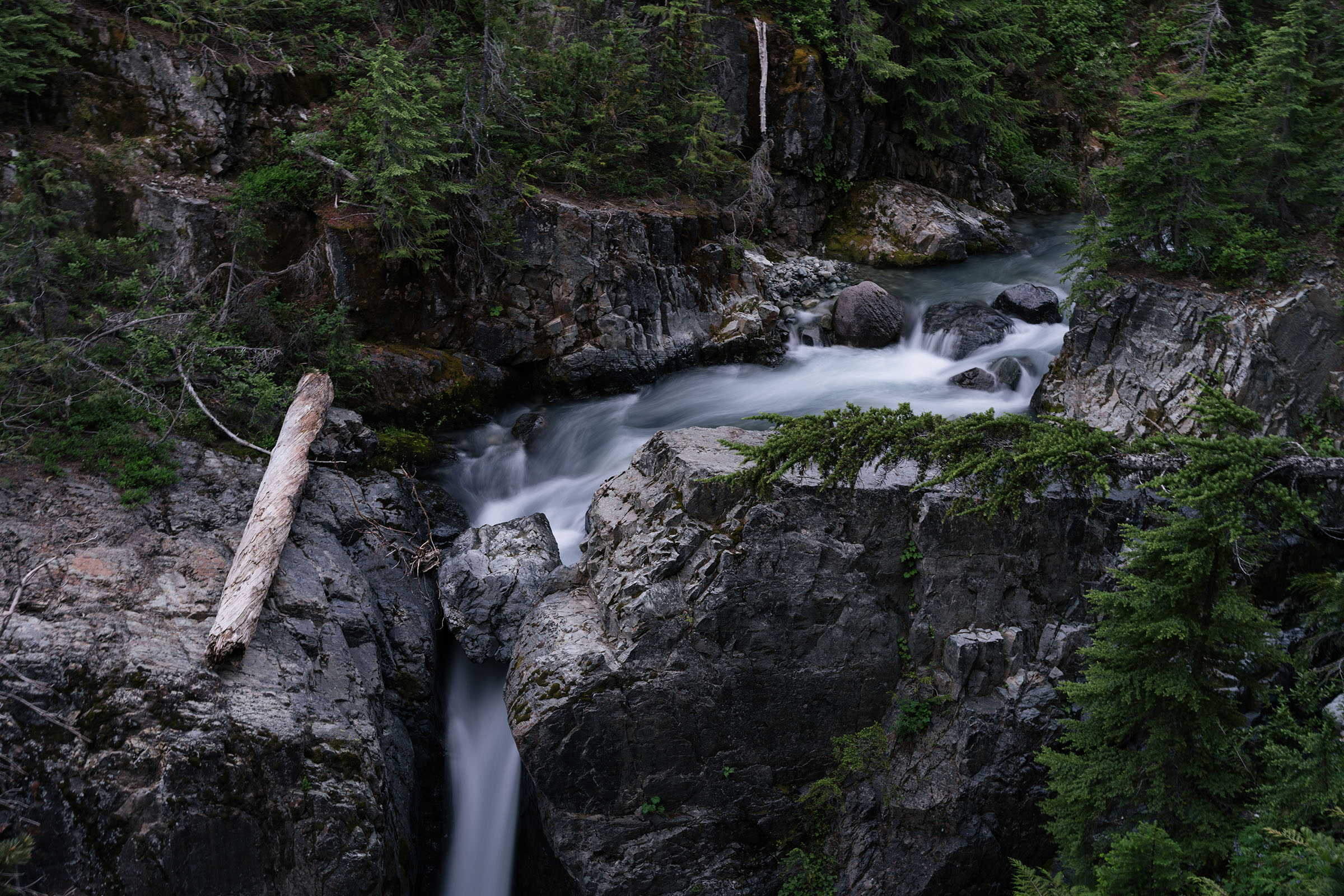 A rocky pool dropping it's water down a cliff outside of the frame in evening light
