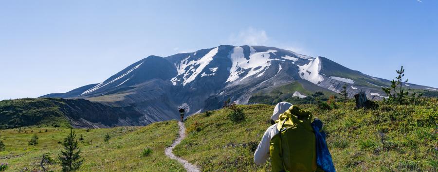 A person walking on a trail towards a large mountain