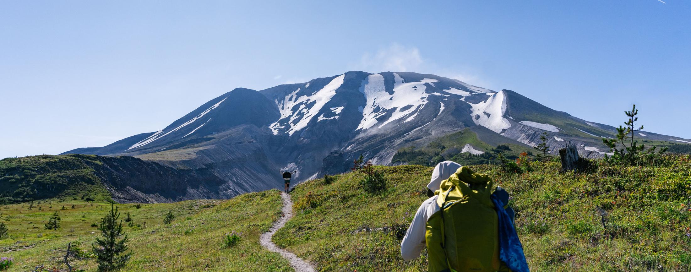 A person walking on a trail towards a large mountain